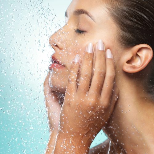 Shot of a young woman taking a shower against a blue background.