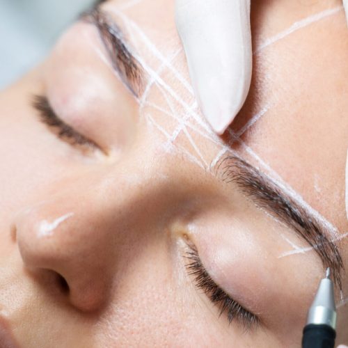 Young woman during professional eyebrow mapping procedure before permanent makeup